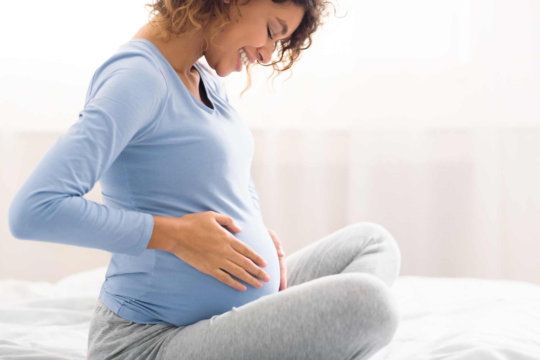 pregnant woman sitting on a bed smiling and holding her stomach